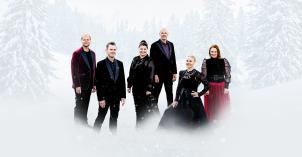 Kuusi esiintyjää seisoo lumisessa metsämaisemassa talvisissa juhla-asuissa. Taustalla näkyy lumisia kuusia ja kuvan alareunassa vaalea lumisumu.