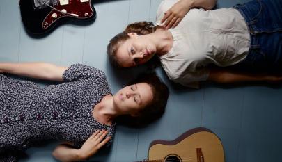 Kaksi naista ja kitaraa lattialla.