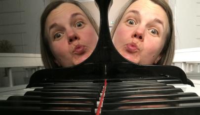 Pianon koskettimet ja naisen kasvot, jotka heijastuvat pianon pinnasta.