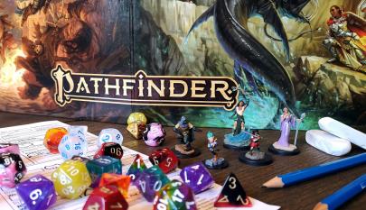 Pathfinder-pelin kansi ja pelaamiseen tarvittavia välineitä.