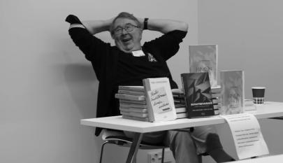 Yksi henkilö istuu pöydän takana. Pöydällä on kirjoja.