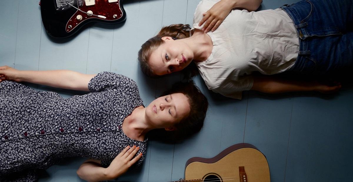 Kaksi naista ja kaksi kitaraa lattialla.