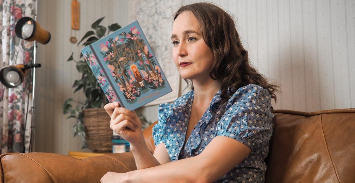 Nainen istuu sohvalla lukemassa kirjaa.
