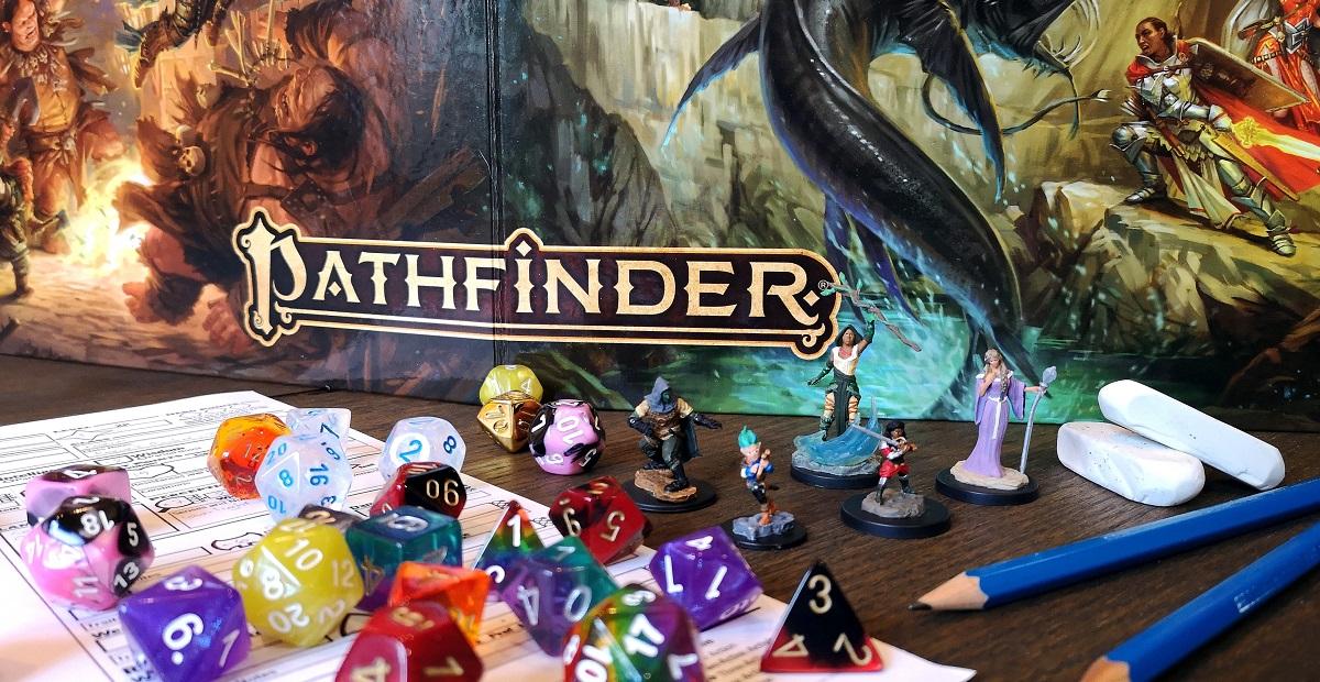 Pathfinder-pelin kansi ja pelaamiseen tarvittavia välineitä.