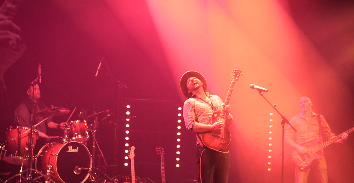 punasävyinen kuva, jossa artisti iloisesti soittaa kitaraa, muita bändin jäseniä taustalla